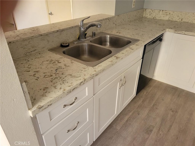 kitchen with sink, white cabinetry, black dishwasher, light stone counters, and wood-type flooring