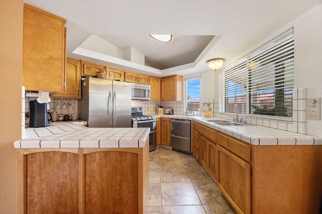 kitchen with stainless steel appliances, tile counters, kitchen peninsula, and a tray ceiling