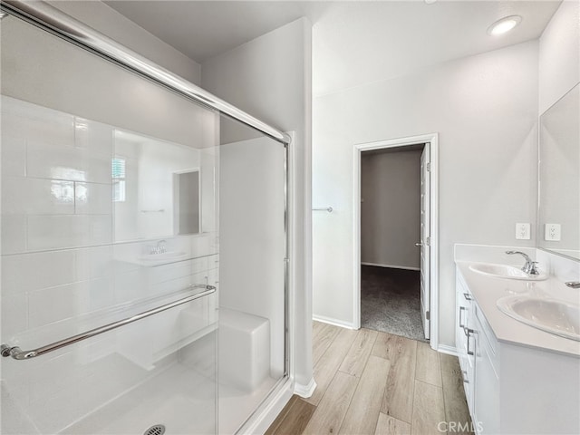 full bathroom with double vanity, a sink, a shower stall, and wood finished floors