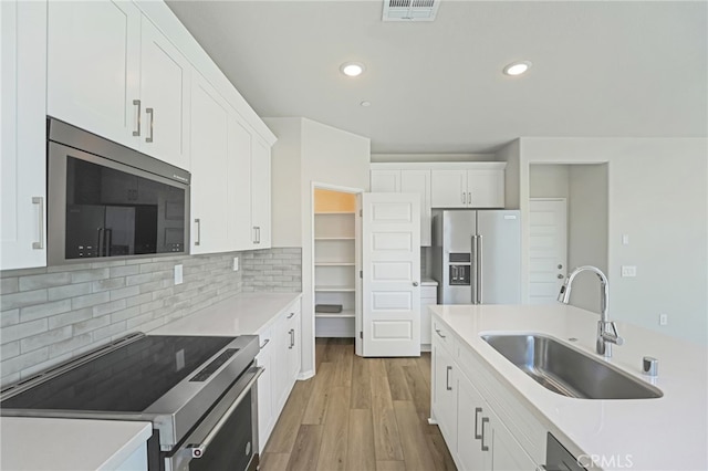 kitchen featuring white cabinets, decorative backsplash, appliances with stainless steel finishes, wood finished floors, and a sink