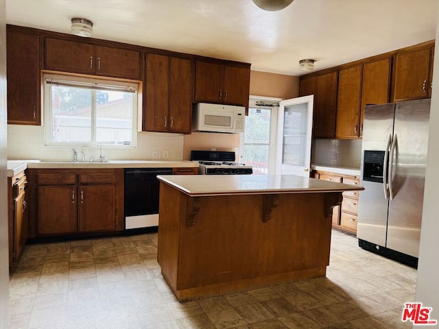 kitchen featuring a kitchen island, a breakfast bar, sink, backsplash, and white appliances