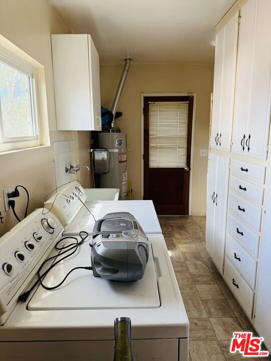 clothes washing area with cabinets, washer / dryer, and secured water heater