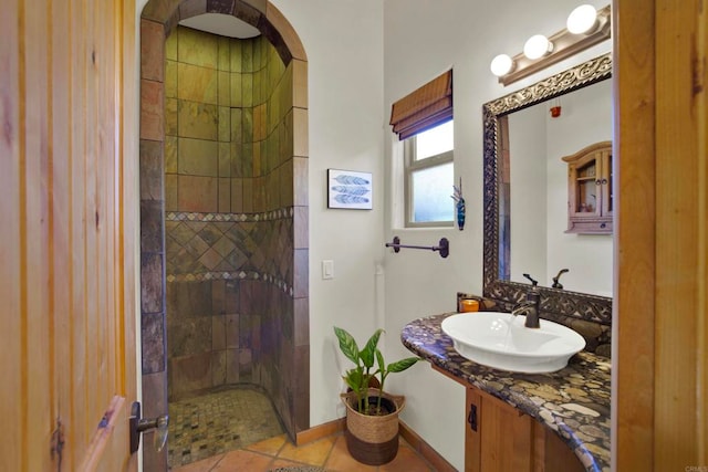 full bathroom featuring a tile shower, baseboards, and a sink