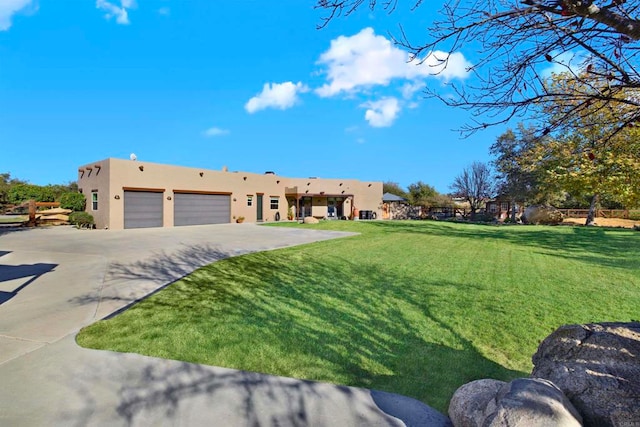 pueblo-style house featuring stucco siding, an attached garage, concrete driveway, and a front yard