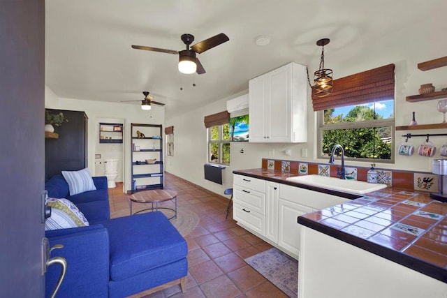 kitchen with white cabinetry, tile counters, dark tile patterned floors, and a sink