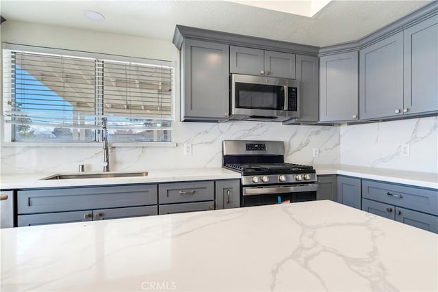 kitchen featuring light stone counters, appliances with stainless steel finishes, gray cabinets, and decorative backsplash