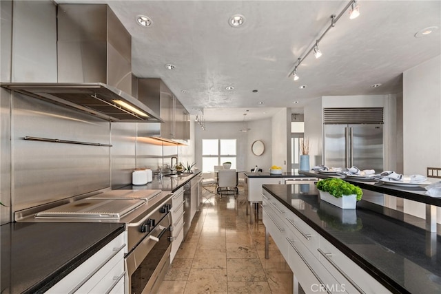 kitchen featuring sink, rail lighting, white cabinetry, stainless steel appliances, and wall chimney exhaust hood