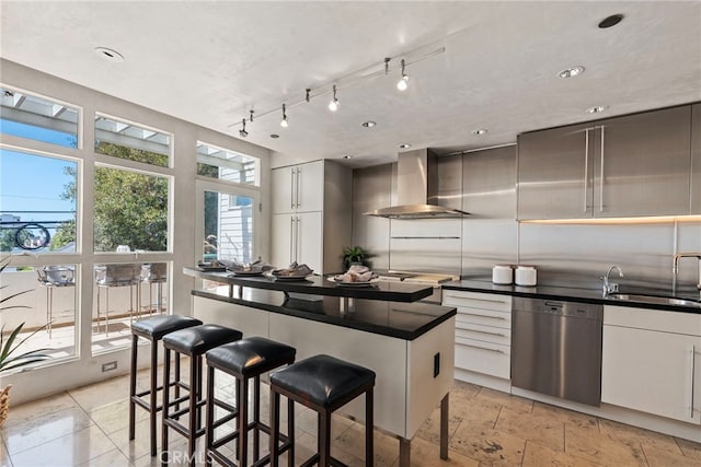 kitchen with sink, a breakfast bar area, dishwasher, white cabinetry, and wall chimney exhaust hood