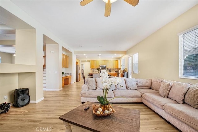 living room with a ceiling fan, plenty of natural light, light wood-style flooring, and baseboards