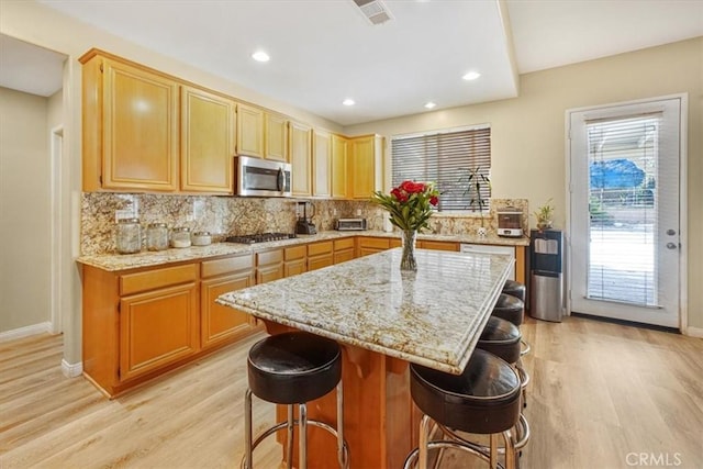 kitchen with light wood-type flooring, a kitchen bar, stainless steel appliances, and a center island