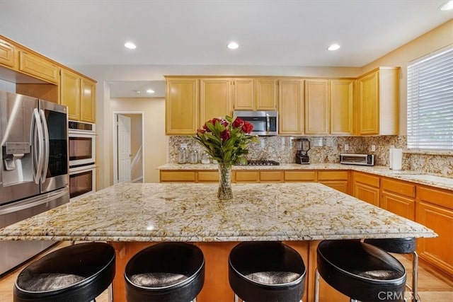 kitchen with appliances with stainless steel finishes, a kitchen bar, light stone countertops, and a center island