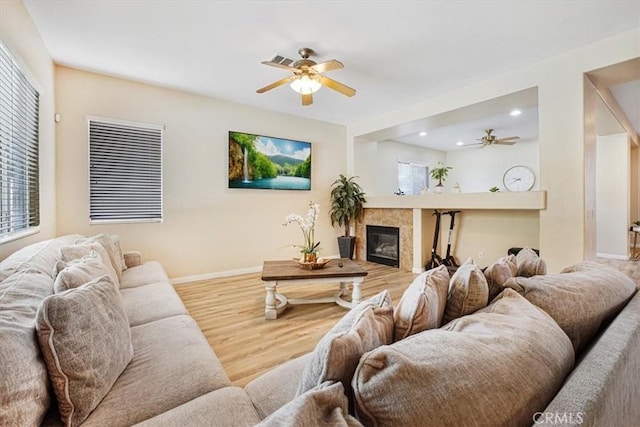 living room featuring visible vents, a tiled fireplace, a ceiling fan, wood finished floors, and baseboards