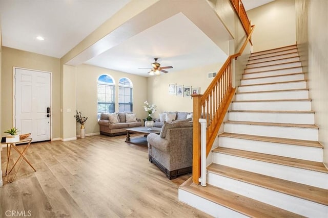 living area featuring light wood finished floors, baseboards, visible vents, ceiling fan, and stairway