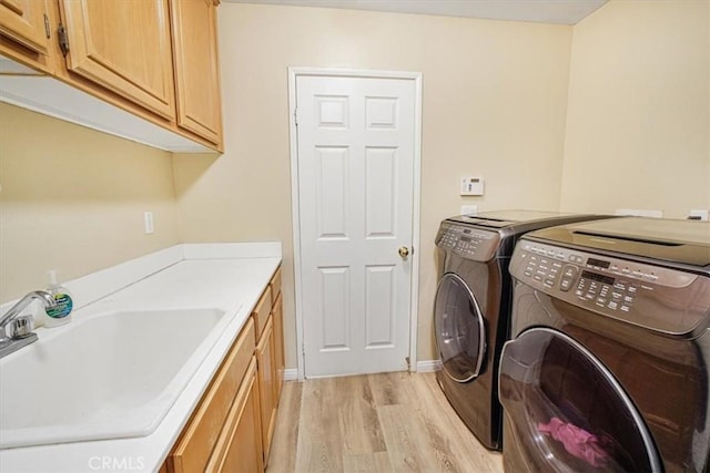 clothes washing area with cabinet space, washing machine and dryer, light wood finished floors, and a sink