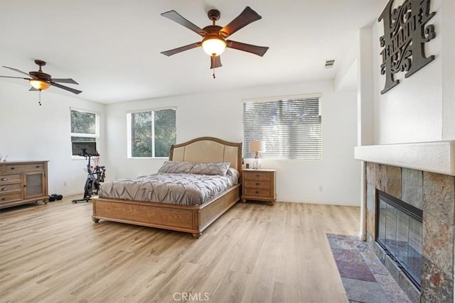 bedroom featuring ceiling fan, a tiled fireplace, visible vents, and light wood-style floors