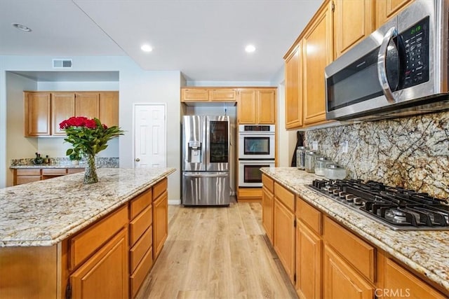 kitchen featuring stainless steel appliances, light wood finished floors, decorative backsplash, and light stone countertops