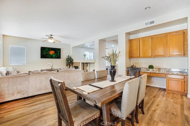 dining space featuring light wood finished floors, built in study area, visible vents, and a ceiling fan