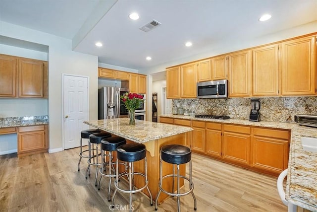 kitchen featuring light wood-style flooring, a kitchen breakfast bar, light stone countertops, stainless steel appliances, and built in desk