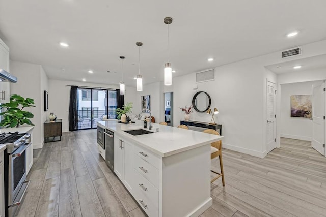 kitchen with white cabinetry, appliances with stainless steel finishes, a kitchen island with sink, and decorative light fixtures