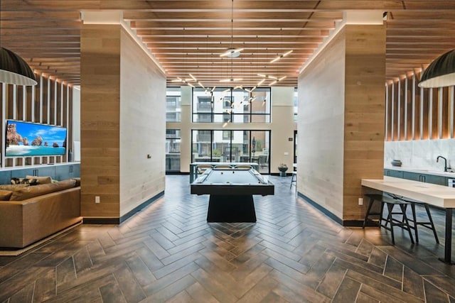 rec room with a high ceiling, dark parquet flooring, and wood walls