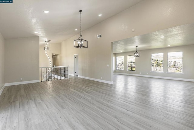 unfurnished living room featuring high vaulted ceiling, a textured ceiling, light hardwood / wood-style floors, and a chandelier