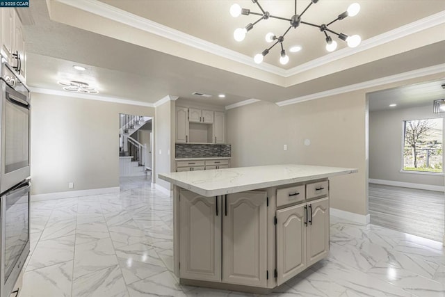 kitchen with tasteful backsplash, crown molding, light stone counters, a raised ceiling, and a kitchen island