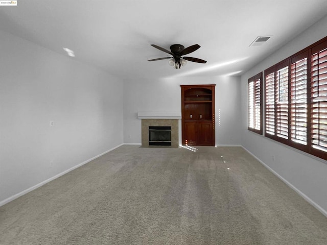 unfurnished living room with a tile fireplace, ceiling fan, and carpet