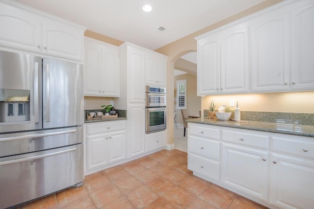 kitchen featuring white cabinetry, light tile patterned floors, stainless steel appliances, and dark stone countertops