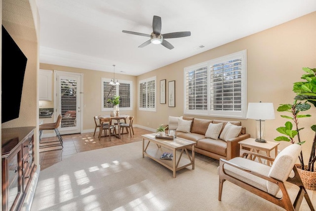 tiled living room with ceiling fan with notable chandelier