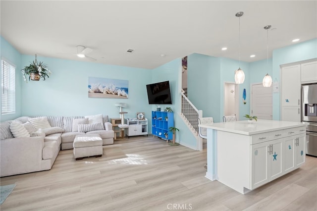 interior space featuring decorative light fixtures, stainless steel fridge, a kitchen island, light hardwood / wood-style floors, and white cabinets