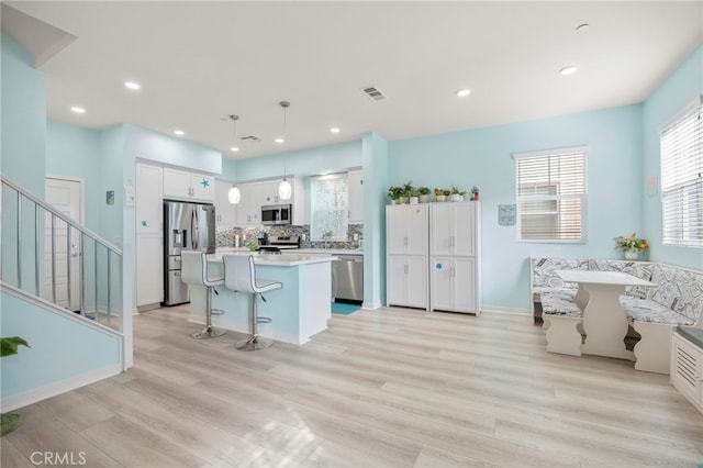 kitchen featuring white cabinetry, a kitchen island, pendant lighting, stainless steel appliances, and light hardwood / wood-style floors