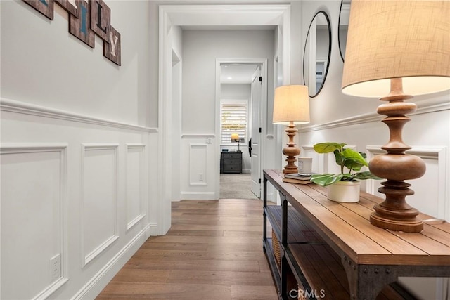 hallway featuring a decorative wall, wainscoting, and wood finished floors