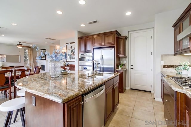 kitchen featuring a kitchen bar, sink, light stone counters, appliances with stainless steel finishes, and an island with sink