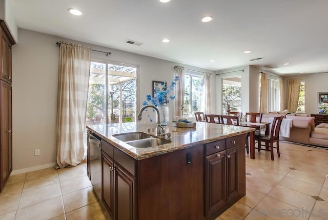 kitchen with light stone counters, sink, an island with sink, and a healthy amount of sunlight