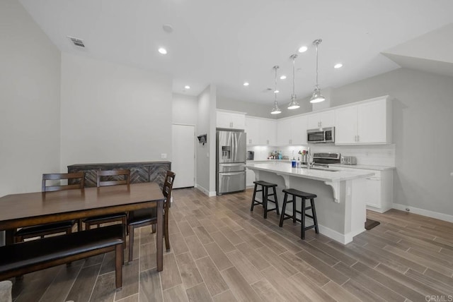 kitchen featuring white cabinetry, hanging light fixtures, a center island with sink, stainless steel appliances, and a kitchen bar