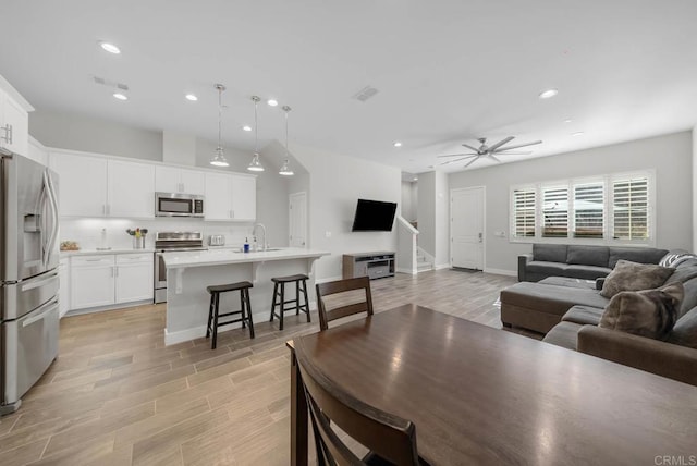 living room with ceiling fan, sink, and light wood-type flooring