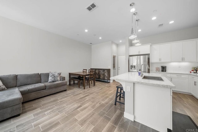 kitchen featuring pendant lighting, white cabinetry, sink, stainless steel refrigerator with ice dispenser, and a center island with sink