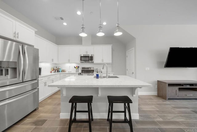 kitchen with appliances with stainless steel finishes, sink, white cabinets, light stone counters, and a center island with sink