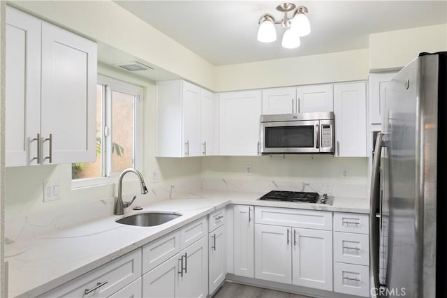 kitchen featuring stainless steel appliances, white cabinets, a sink, and light stone countertops