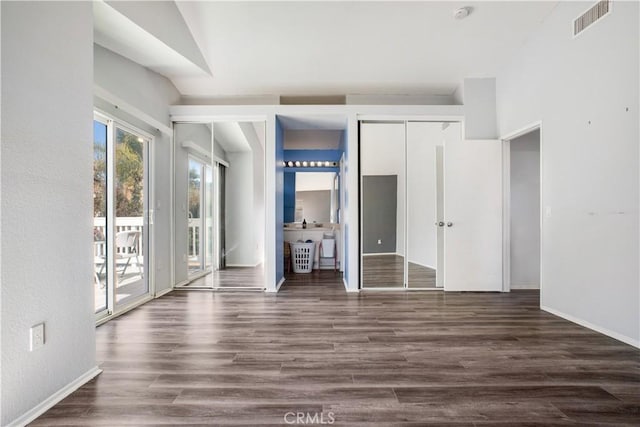 unfurnished bedroom featuring dark wood-style flooring, two closets, visible vents, and access to exterior