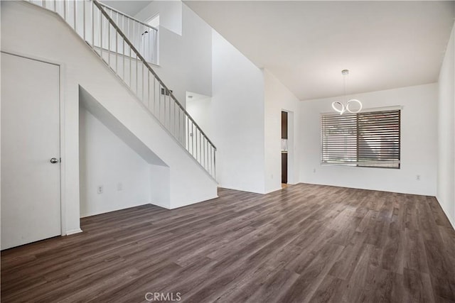 unfurnished living room with stairs, a high ceiling, dark wood finished floors, and an inviting chandelier