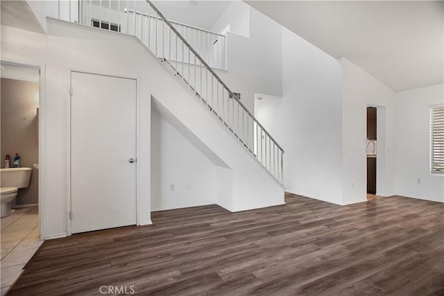 unfurnished living room featuring dark wood-type flooring, stairway, and a high ceiling