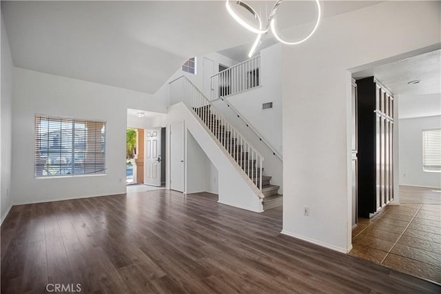 unfurnished living room with dark wood-style floors, visible vents, stairway, a towering ceiling, and baseboards