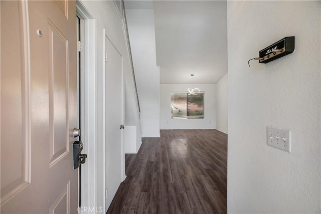 hall featuring dark wood-type flooring and an inviting chandelier