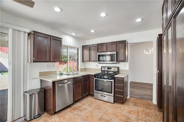 kitchen featuring dark brown cabinetry, recessed lighting, stainless steel appliances, a sink, and light countertops