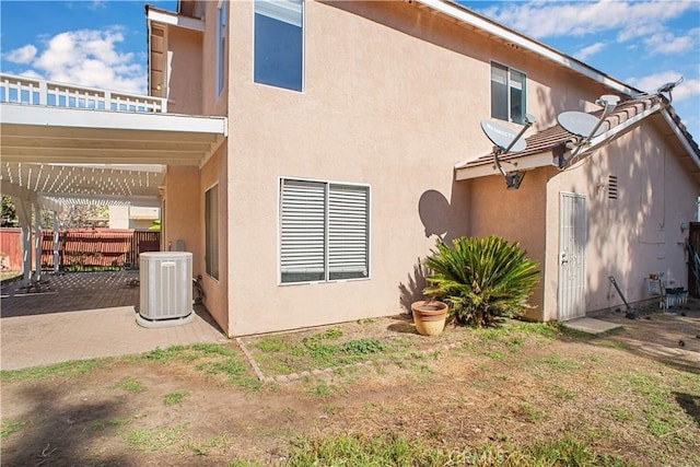 rear view of property featuring a pergola, stucco siding, fence, and central air condition unit