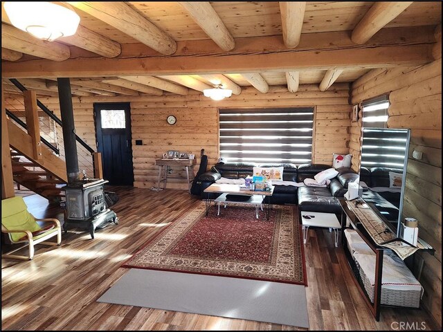 living room featuring dark wood-type flooring, rustic walls, beam ceiling, wooden ceiling, and a wood stove