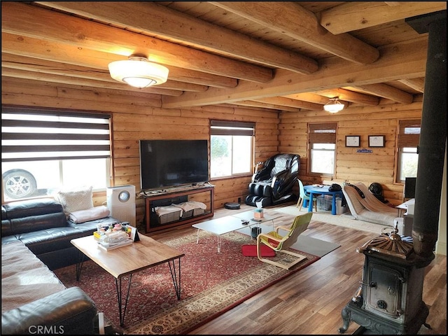 living room with wood walls, wood-type flooring, beam ceiling, and a wood stove