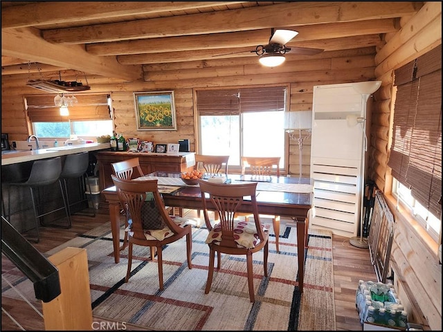 dining area with beamed ceiling, ceiling fan, wooden walls, and light hardwood / wood-style floors