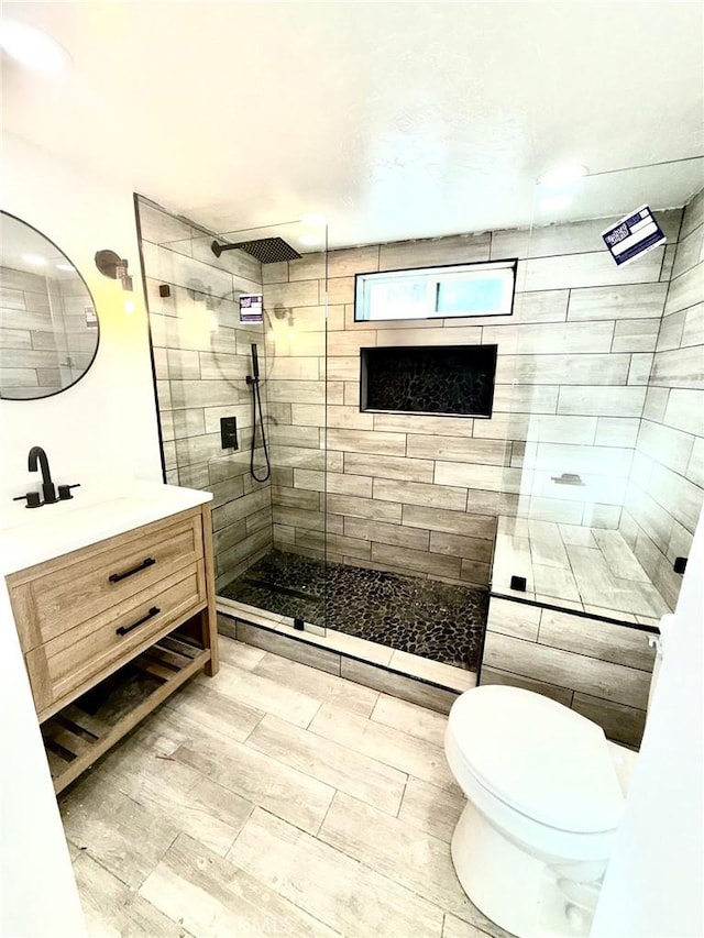 bathroom with vanity, toilet, wood-type flooring, and a tile shower